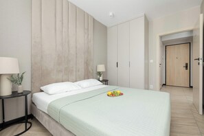 Une chambre d’hôtel comprenant un lit, des tables de chevet, une lampe, un panier de fruits et une armoire.