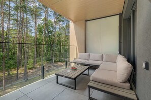 Ein moderner Sitzbereich im Freien mit einer Couch und einem Tisch, mit Blick auf ein bewaldetes Gebiet.