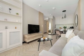 Ein modernes Wohnzimmer mit Fernseher, Sofa, Couchtisch und einem Essbereich mit Tisch und Stühlen.