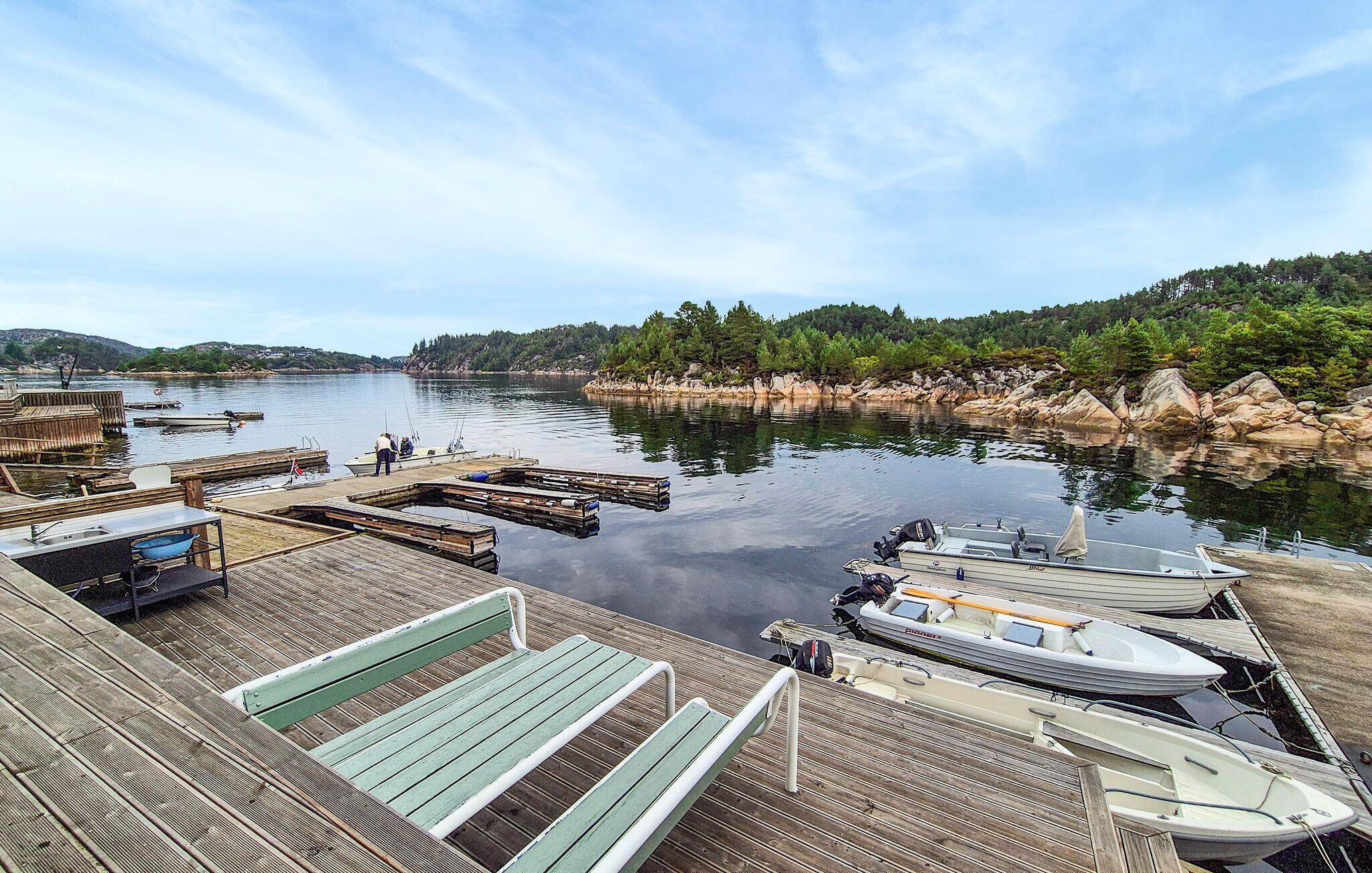 Un quai avec des bateaux, une terrasse en bois et une vue sur une rivière paisible, avec des arbres en arrière-plan.