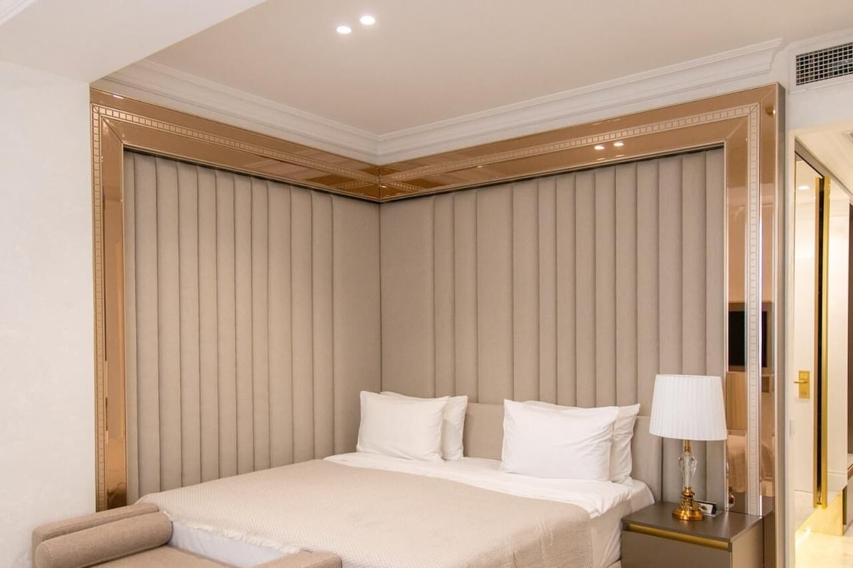 Una habitación de hotel con una cama grande, mesitas de noche, una lámpara y un espejo.