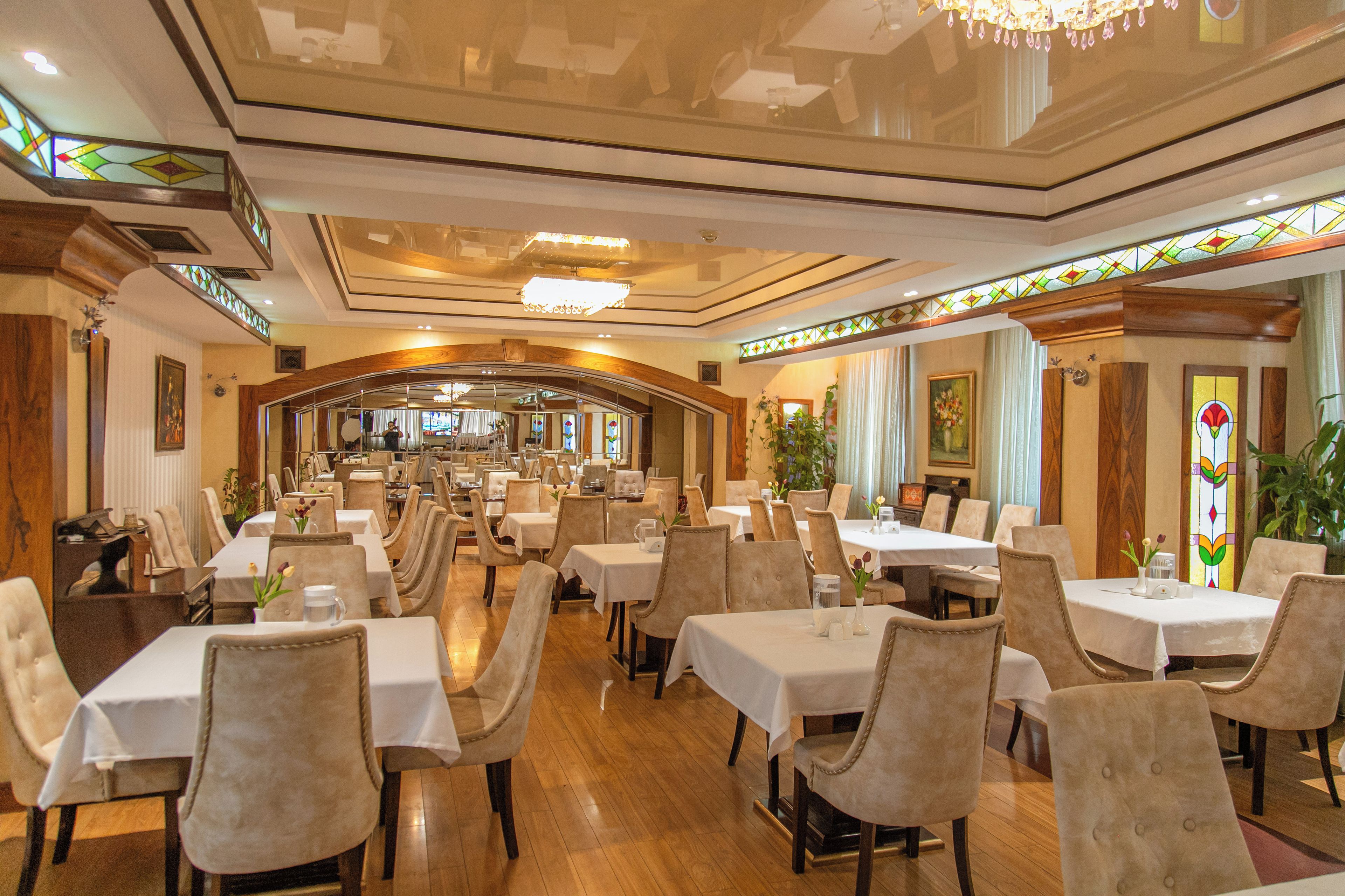 Un restaurante espacioso con varias mesas y sillas, un techo alto con detalles decorativos y vistas al área de comedor.