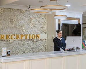 A reception desk with a 'RECEPTION' sign, a patterned wall, and a modern chandelier. - GPH Baku (Baku)
