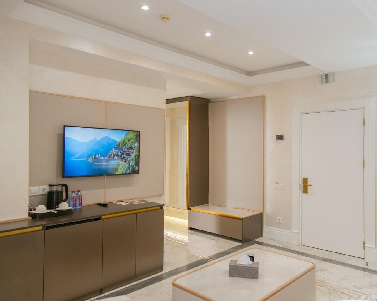A hotel lobby with a reception desk, a television displaying a scenic view, a white door, and a marble floor.