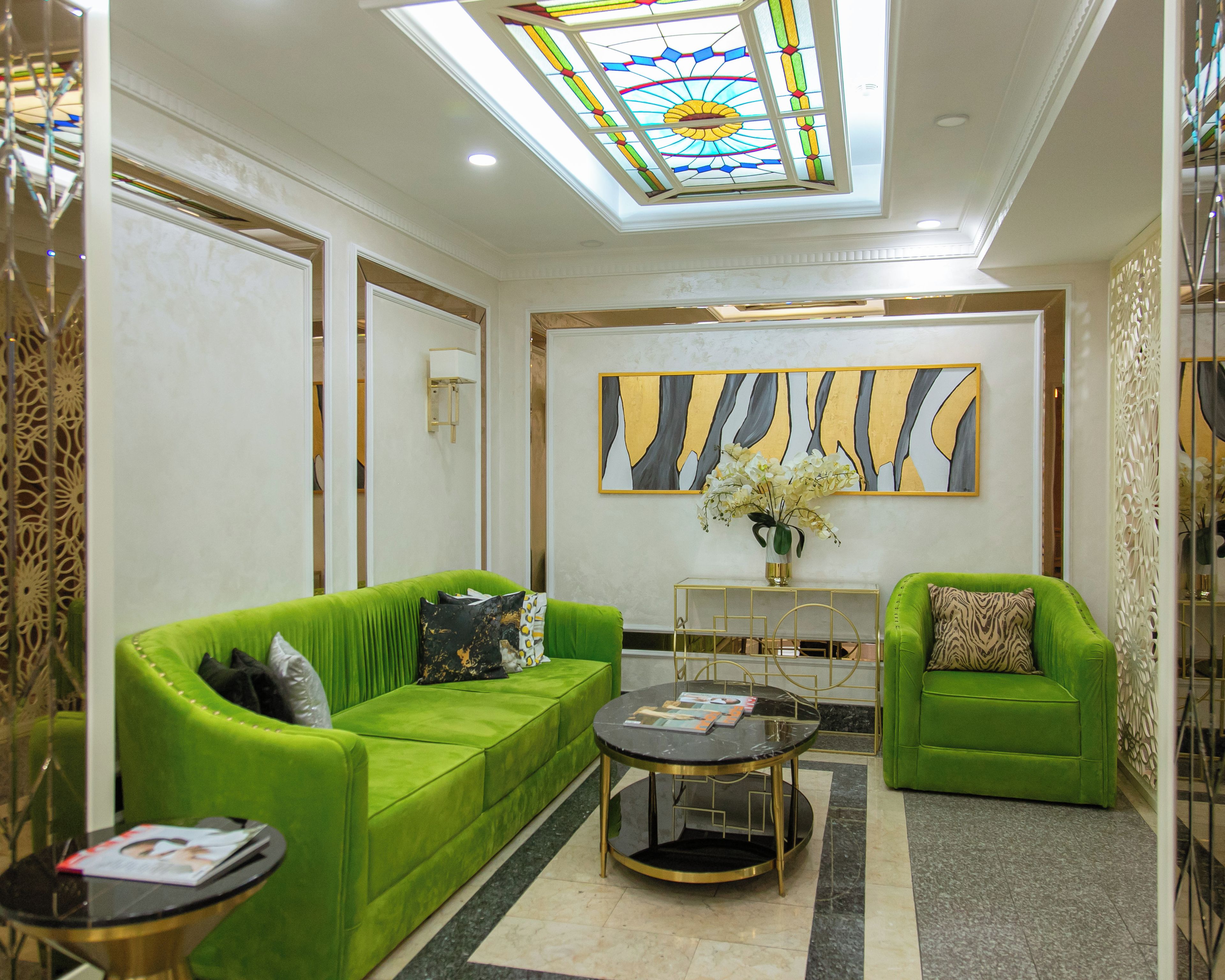 A modern living room with green sofas, a round coffee table, and a large abstract painting on the wall.