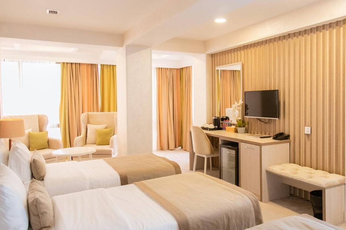 Habitación de hotel con dos camas, un escritorio, un televisor y una pequeña kitchenette.