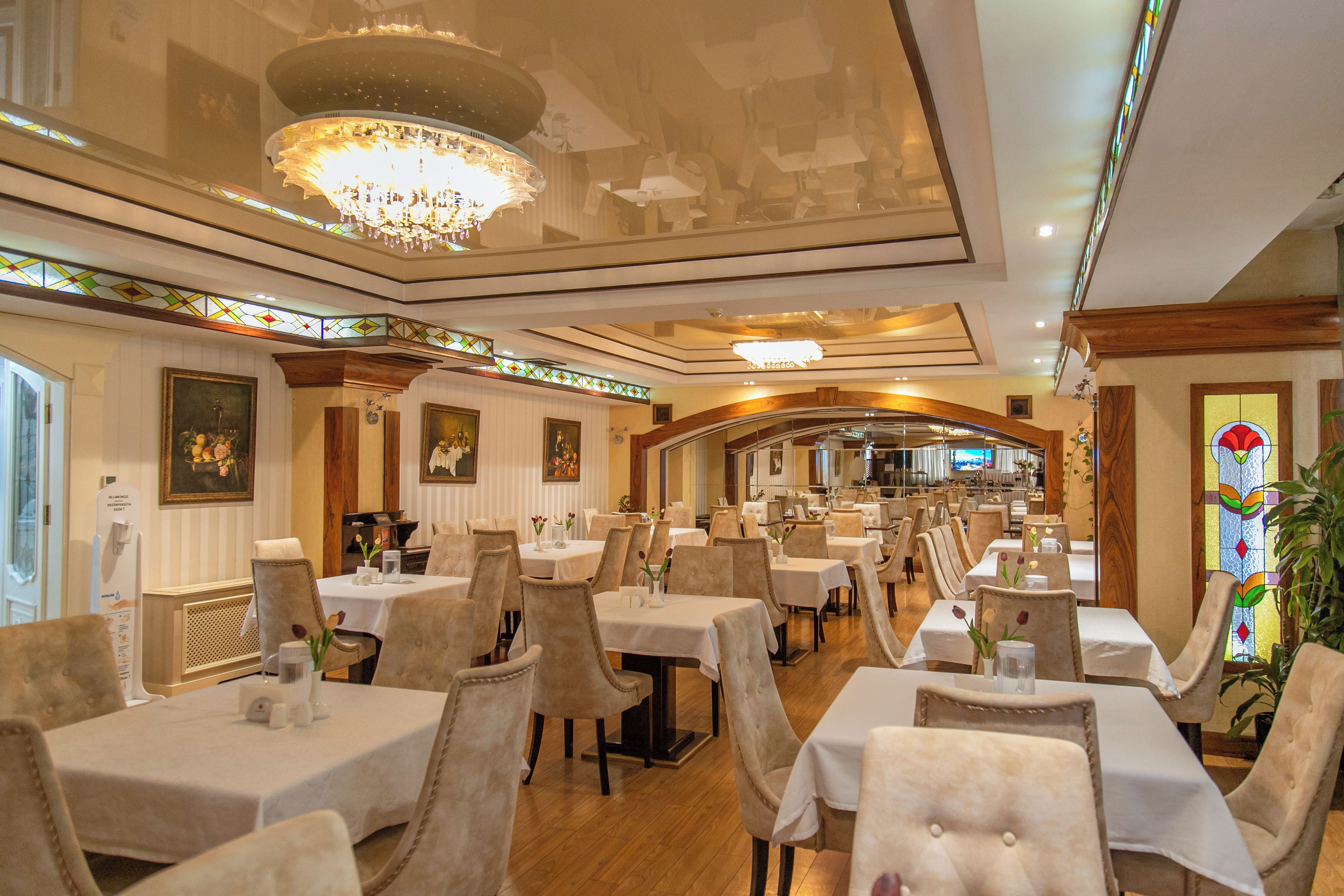 A restaurant with multiple tables and chairs, a chandelier, and a stained glass window.