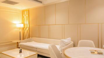 A hotel room with a sofa, a round table, a lamp, and a small bedside table.