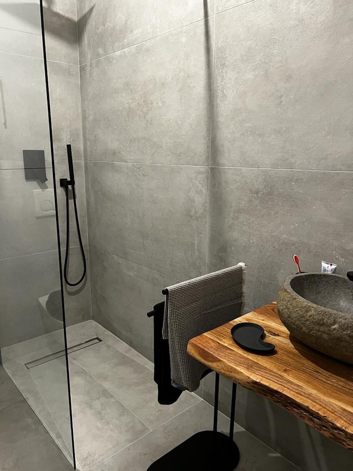 Une salle de bain moderne avec une douche, une table en bois surmontée d’un lavabo en pierre et un porte-serviettes.