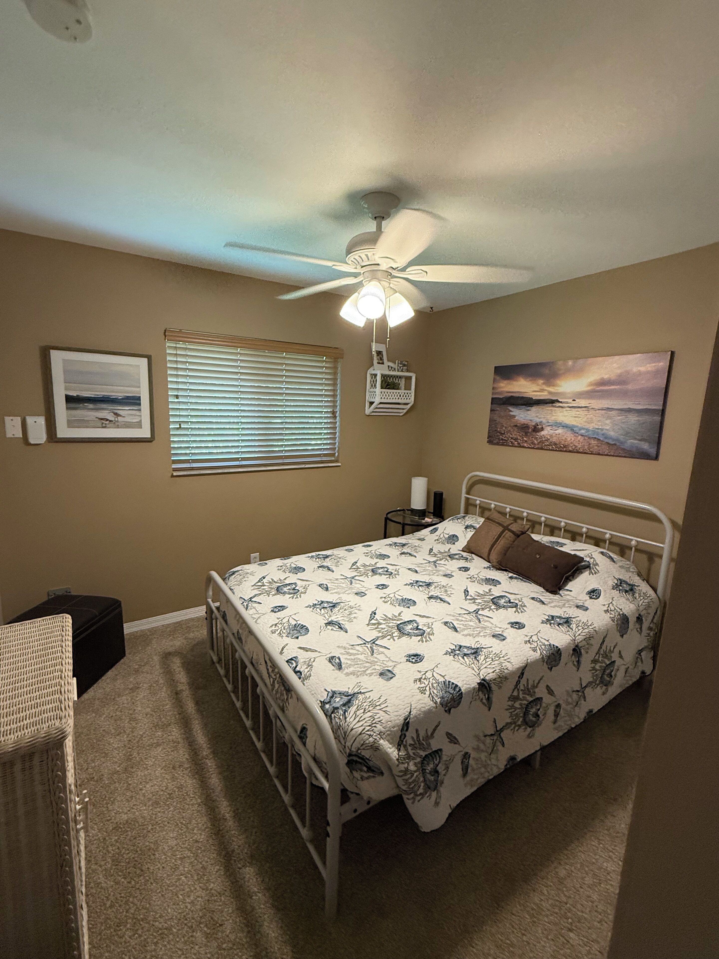 A bedroom with a bed, a ceiling fan, a window with blinds, and a wall-mounted light fixture.