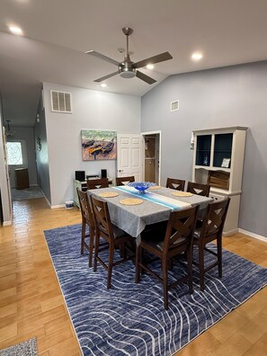 Un coin repas avec une table dressée pour quatre personnes, un ventilateur de plafond et un tableau accroché au mur.