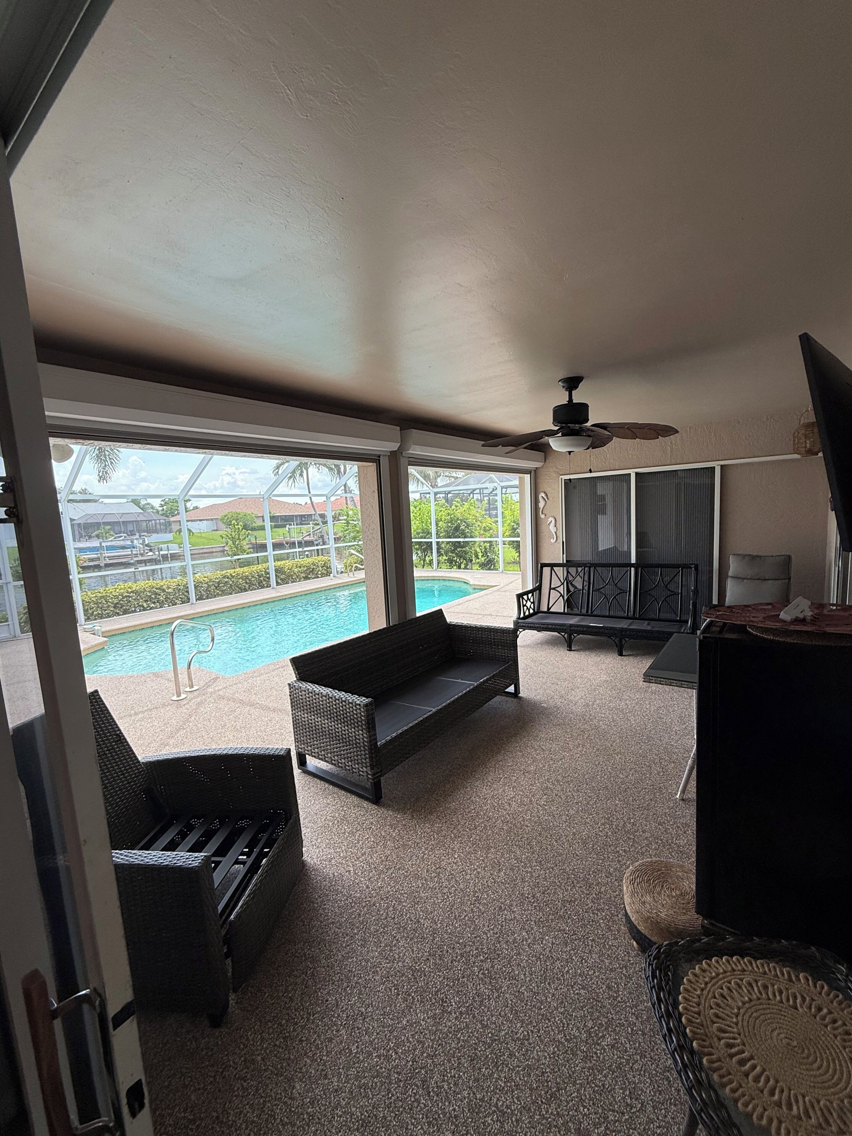 A room with a large window overlooking a swimming pool, a ceiling fan, and a television.