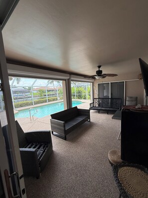 Une chambre dotée d’une grande fenêtre donnant sur une piscine, d’un ventilateur de plafond et d’un téléviseur.