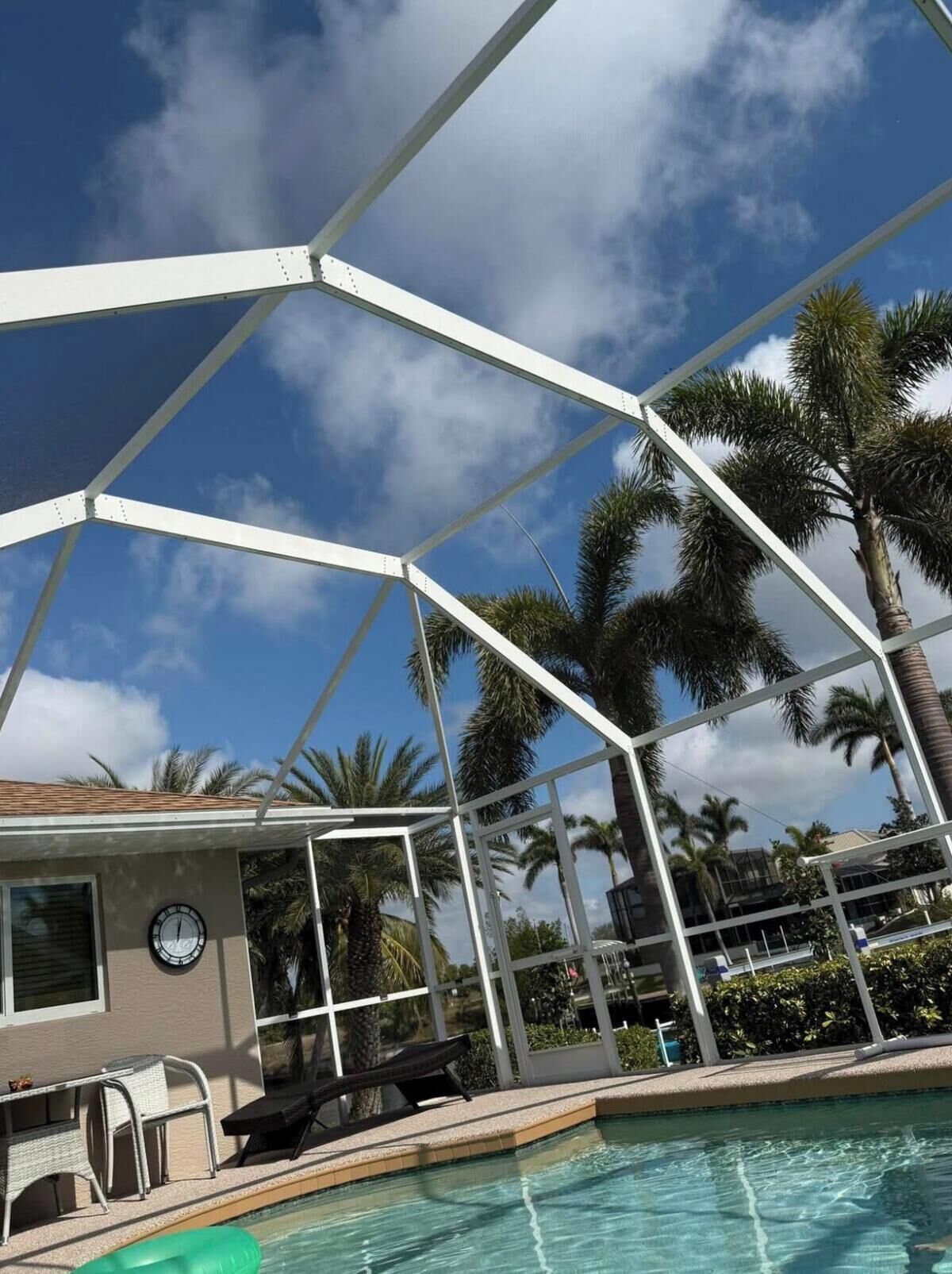 A pool area with a covered seating area, palm trees, and a clear sky.