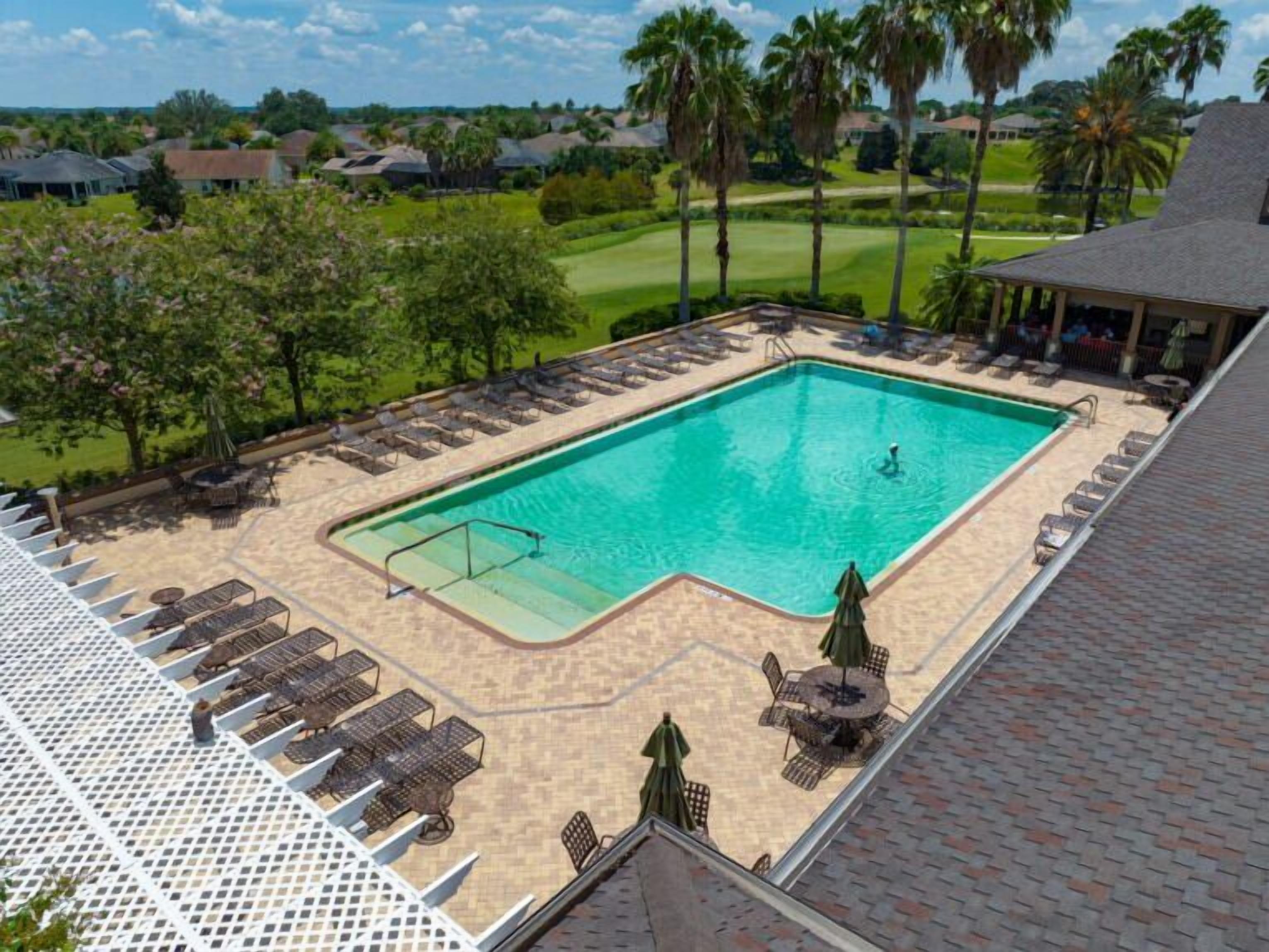 Una piscina rectangular con una terraza perimetral, sillas de descanso y sombrillas.