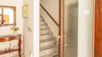 Eine Treppe mit Marmorstufen führt zu einer Empore, eine Holztür mit gefrostetem Glasfeld, ein Konsolentisch mit einer Vase und ein wandmontiertes Telefon.