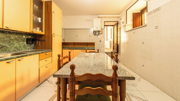 Uma cozinha com bancada de mármore, armários de madeira e uma mesa de jantar comprida.