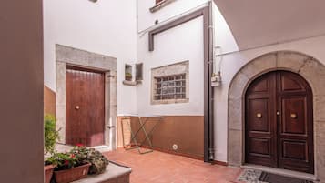 Ein Innenhof mit Terrakotta-Fliesen, einer Holztür und einem steinernen Bogen.