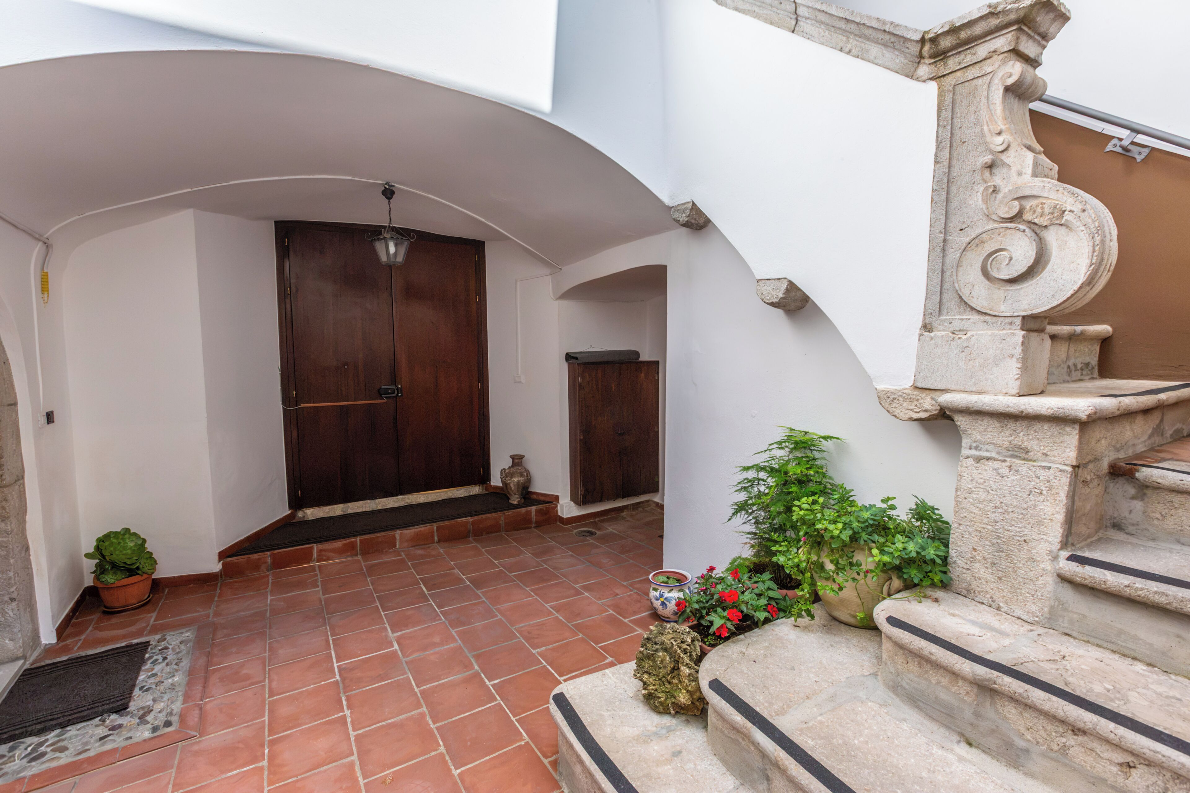 Un patio con puerta de madera, escaleras de piedra y plantas en macetas.