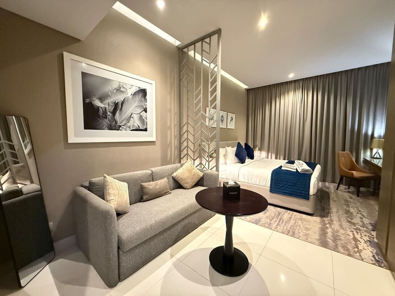 Ein Hotelzimmer mit einer Couch, einem runden Tisch, einem Bett mit blauer Decke und einem großen gerahmten Bild an der Wand.