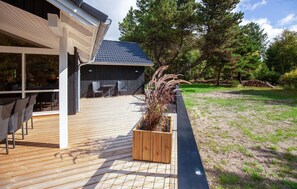En træterrasse med udendørs møbler, en overdækket patio og en have med en træplantekasse.