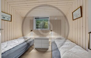 Een kamer met twee eenpersoonsbedden, een kleine witte ladekast en een raam met uitzicht op bomen.