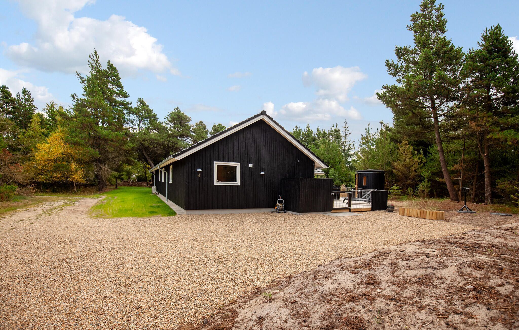 A black building with a gravel driveway, surrounded by trees and a clear sky.