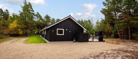A black building with a gravel driveway, surrounded by trees and a clear sky.