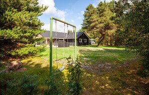 Ein grünes Areal im Freien mit einer Schaukel, einer Holzkonstruktion und Bäumen.