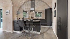 A modern kitchen with a central island, bar stools, and a large refrigerator. - Beautiful home in Blåvand with sauna (Blåvand)