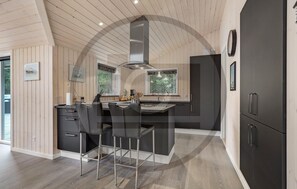 A modern kitchen with a central island, bar stools, and a large refrigerator. - Beautiful home in Blåvand with sauna (Blåvand)