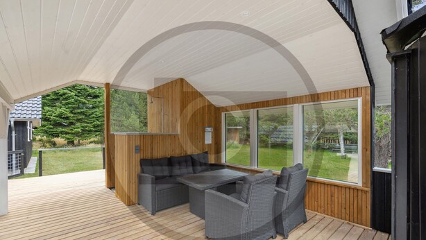 An outdoor patio with a wooden deck, a built-in sofa, and a table. - Beautiful home in Blåvand with sauna (Blåvand)