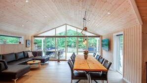 A spacious room with a wooden ceiling, a large dining table with chairs, a sofa, and a television mounted on the wall. - Beautiful home in Blåvand with sauna (Blåvand)