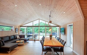 A spacious room with a wooden ceiling, a large dining table with chairs, a sofa, and a television mounted on the wall. - Beautiful home in Blåvand with sauna (Blåvand)