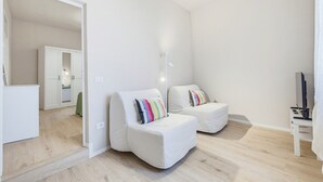 Ein modernes Wohnzimmer mit einem weißen Sofagarnitur, einem Flachbildfernseher und einer Deckenleuchte.