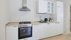 Eine moderne Küche mit weißen Schränken, einer Edelstahl-Dunstabzugshaube, einem eingebauten Backofen und einer Arbeitsplatte mit einer Kaffeemaschine und weiteren Gegenständen.