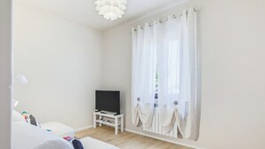 Ein Zimmer mit einem Bett, einem Fernseher auf einem Schrank und einem Fenster mit durchsichtigen Vorhängen.