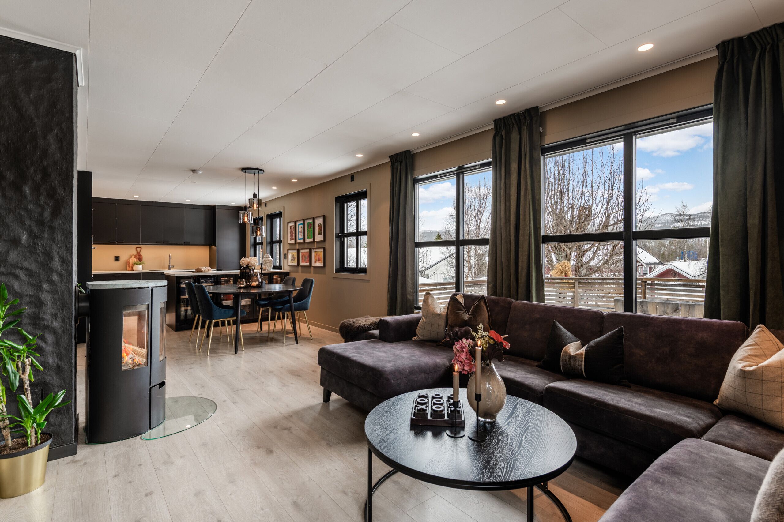 A modern living room with a fireplace, a dining area, and large windows offering a view of the outdoors.
