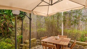 Terrassa exterior amb taula i cadires de fusta, una paraigua beix i una tanca de bambú.