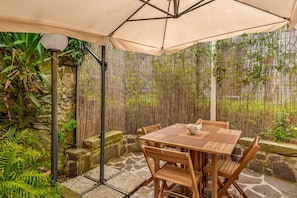 An outdoor patio with a wooden table and chairs, a beige umbrella, and a bamboo fence. - [IlGelsomino] Biassa-5Terre+A/C+ bus for 5 terre (Biassa)