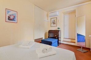 Une chambre d’hôtel comprenant un lit, un bureau, une chaise, une petite table, un miroir et une porte donnant sur une autre pièce.