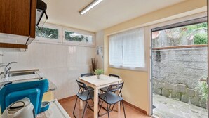 Cuina compacta amb zona de dinar, fogó de forn incorporat i finestra amb vista a una paret de pedra.