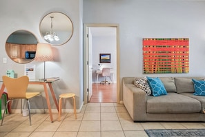 A living room with a sofa, a dining area with a table and chairs, a kitchen area with cabinets and a microwave, and a hallway leading to another room.