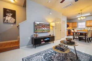 Ein Wohnzimmer mit Flachbildfernseher, Couchtisch mit Büchern, einem gemusterten Teppich und einer Treppe, die zu einer weiteren Ebene führt.