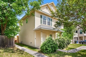 A two-story residential house with a front porch, a small front yard, and a wooden fence.