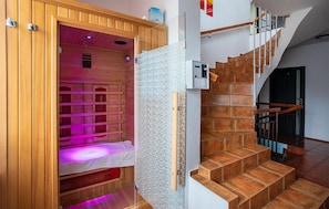A wooden sauna with a bench and a glass partition, adjacent to a staircase with wooden steps and metal railings. - Cozy apartment in Jastrzebia Gora with sauna (Jastrzebia Gora)