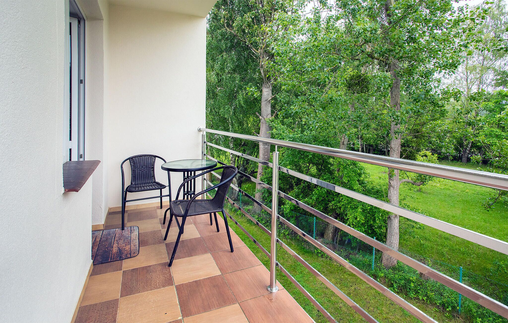 A balcony with two chairs and a table, a metal railing, and a view of a green landscape.