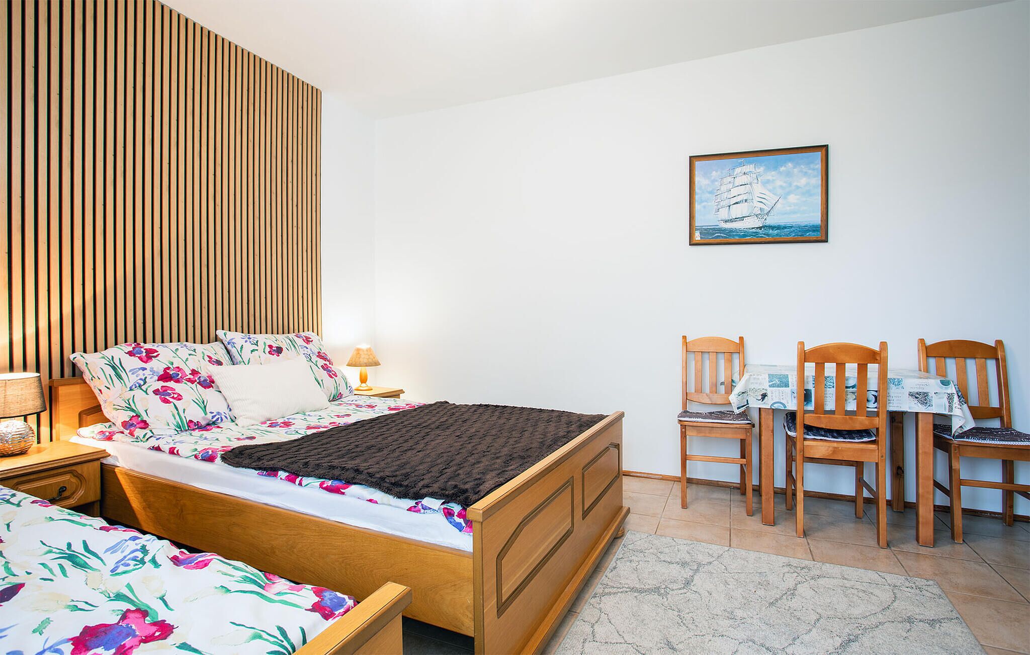 Un dormitorio con cama, un escritorio con sillas, una lámpara y un cuadro en la pared.