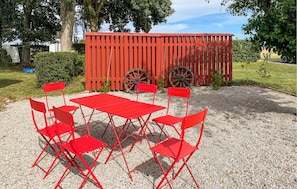 A red outdoor seating area with tables and chairs, a wooden fence, and a wheelbarrow in the background. - Awesome home in Tomelilla with WiFi (Tomelilla)