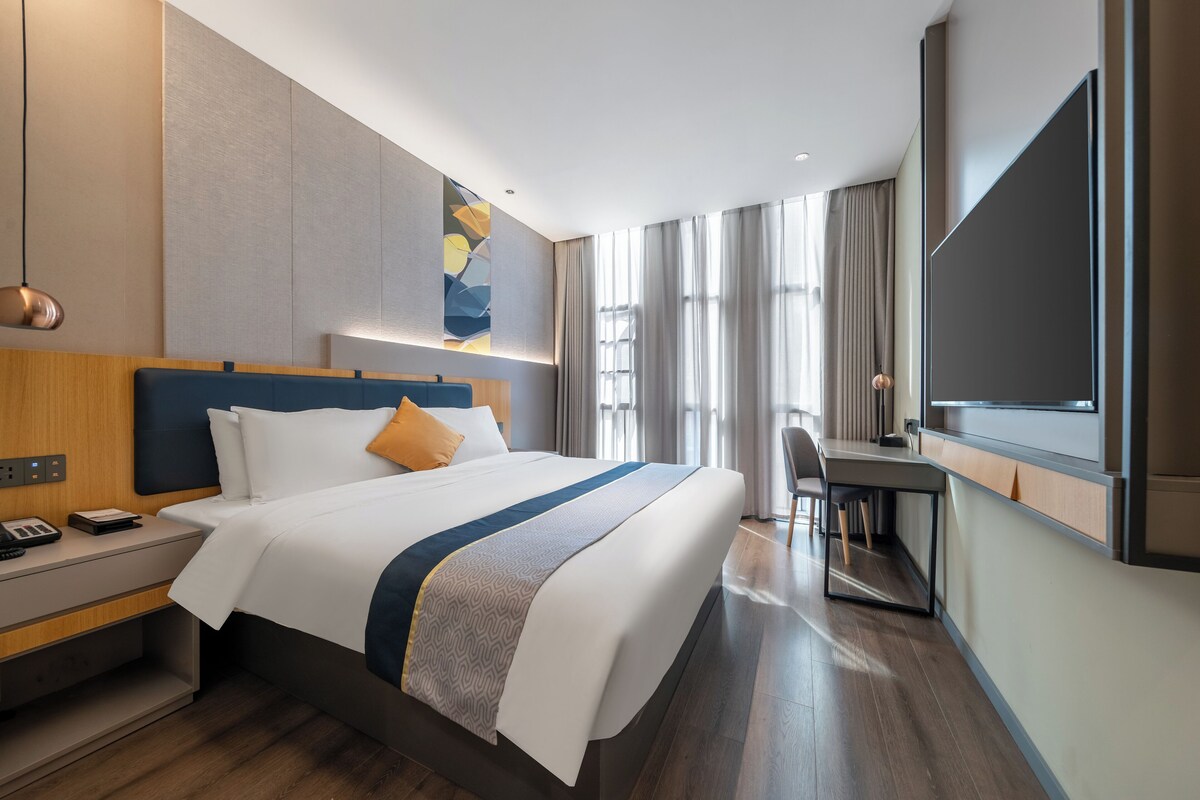 A modern hotel room with a large bed, a desk, and a television.